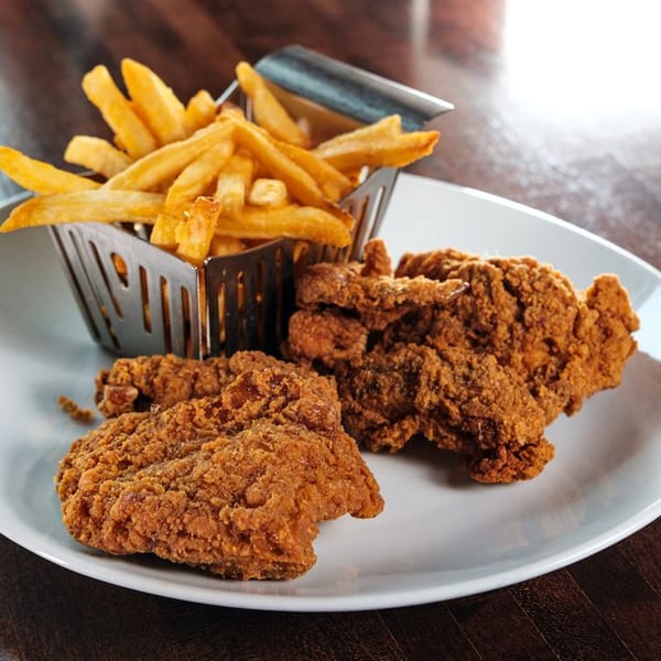 Crispy fried chicken pieces and a metal basket of golden french fries on a white plate.